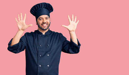Young hispanic man wearing cooker uniform showing and pointing up with fingers number ten while smiling confident and happy.