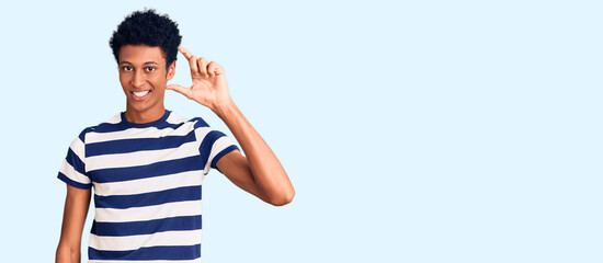 Young african american man wearing casual clothes smiling and confident gesturing with hand doing small size sign with fingers looking and the camera. measure concept.