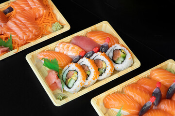 Fresh futomaki sushi takeaway container trays on black background table surface.