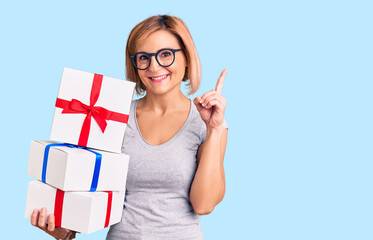 Young blonde woman wearing glasses holding gift surprised with an idea or question pointing finger with happy face, number one