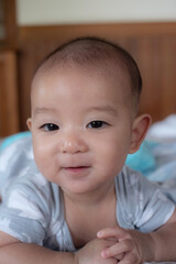 Portrait of happy small Asian infant baby. Kid is lying, smiling, playing on the bed