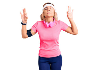 Fototapeta na wymiar Young blonde woman wearing sportswear and headphones relax and smiling with eyes closed doing meditation gesture with fingers. yoga concept.
