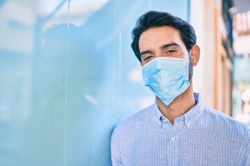 Young hispanic man wearing medical mask leaning on the wall at the city.