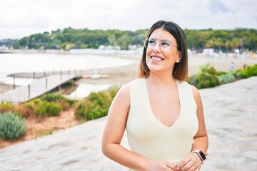 Young beautiful woman smiling happy. Standing with smile on face looking to the side at beach promenade