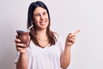 Young beautiful brunette woman drinking mate infusion beverage over white background smiling happy...