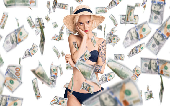 Young blonde woman with tattoo wearing bikini and summer hat thinking looking tired and bored with depression problems with crossed arms.