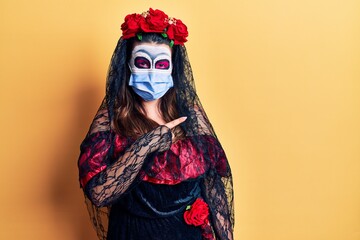 Young woman wearing day of the dead costume wearing medical mask smiling happy pointing with hand and finger to the side