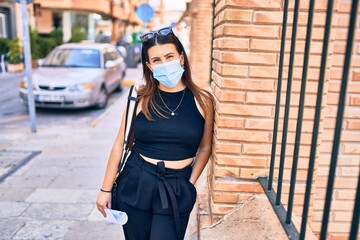 Young beautiful brunette woman wearing medical mask. Standing at town street leaning on the wall