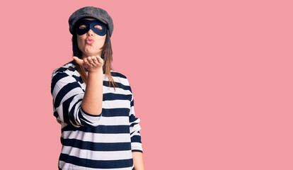 Young beautiful brunette woman wearing burglar mask looking at the camera blowing a kiss with hand on air being lovely and sexy. love expression.