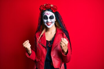 Woman wearing day of the dead costume over red very happy and excited doing winner gesture with arms raised, smiling and screaming for success. celebration concept.