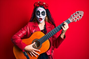 Woman wearing day of the dead costume playing classical guitar afraid and shocked with surprise and amazed expression, fear and excited face.