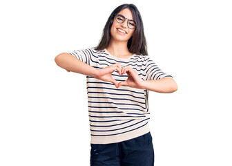 Brunette teenager girl wearing casual clothes and glasses smiling in love doing heart symbol shape with hands. romantic concept.