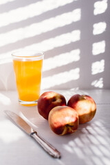 peaches on white wood with American blind light with glass juice glass and a knife next to it