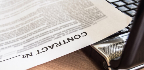 A sheet of paper with a printed contract lying in the office on a wooden table with a laptop