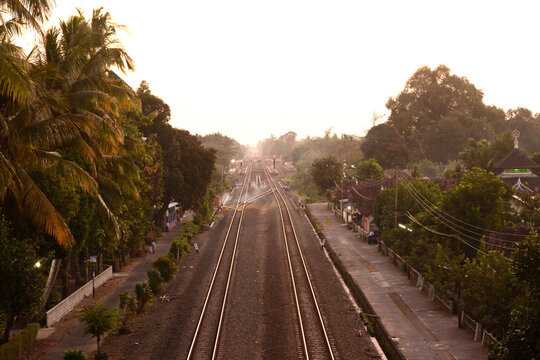 train road in the afternoon with silhouettes of trees and orange sky