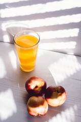 peaches on white wood with American blind light with glass juice glass and a knife next to it