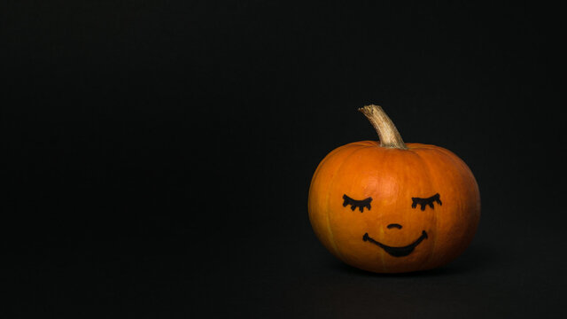 Pumpkin with a painted face on a black background.