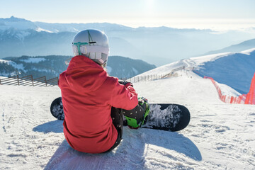 Rear view of snowboarder in sportswear with equipment resting on top of ski slope