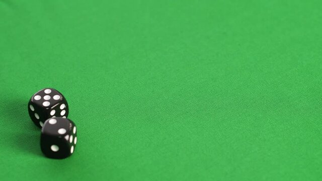 Gambler rolling black dice on green game table in casino close up. Male hands throwing double dice five and two in gambling