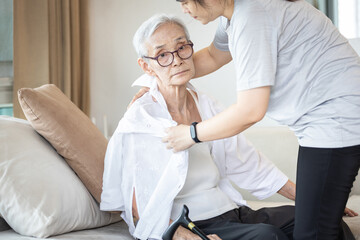 Assisting in dressing,asian female caregiver taking care of helping senior woman get dress,chang clothes for old mother,Alzheimer  elderly patient sit on the sofa at home,preparing go to the hospital.