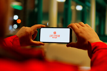 A man watches a live broadcast on a smartphone screen. Button Live Stream on the screen of a mobile phone.