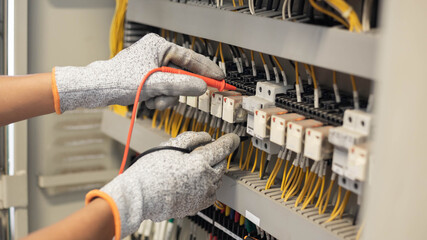 Electrician engineer uses a multimeter to test the electrical installation and power line current in an electrical system control cabinet.