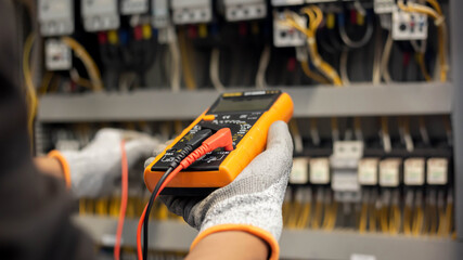 Electrician engineer uses a multimeter to test the electrical installation and power line current in an electrical system control cabinet.