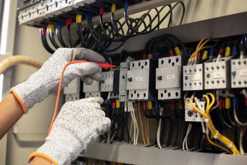 Electrician engineer uses a multimeter to test the electrical installation and power line current in an electrical system control cabinet.