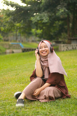 Asian muslim woman with hijab listening to music on headphones. Joyful woman listening to music.