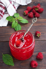 Homemade raspberry jam in a glass jar and fresh raspberries with mint on a wooden rustic background. Copy space