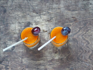 Natural products idea. Glass of plum juice or smoothie with paper straw on wooden natural table with fresh plums.