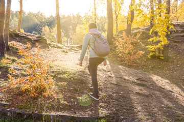 Hiking concept. Hipster young woman with hiking backpack goes walks among the hills,  back view. Climbs mountains in sunny rays. Backlight. Activity tourism