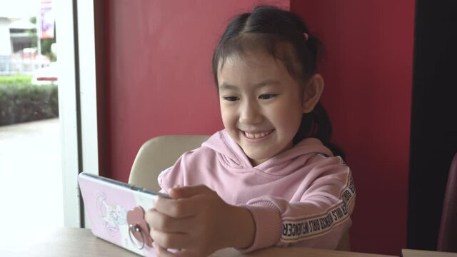 little kid using a smart phone and having a video call chatting or taking a selfie sitting  fun and enjoying online communication