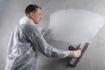 applying, for workers in protective uniforms, finishing putty on a concrete wall, there is a place...