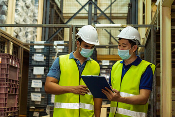 Group of young factory warehouse workers wearing a protective face mask while working in logistic industry indoor. Asian and Indian ethnic men checking item order during Coronavirus Covid 19 pandemic