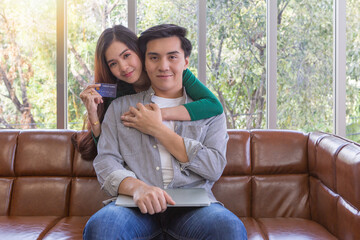 Obraz premium Asian man and woman smiling and showing credit card in living room