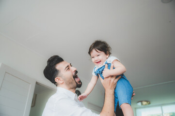 Cheerful young father holding up excited little boy while spending time together and having fun in light room at home