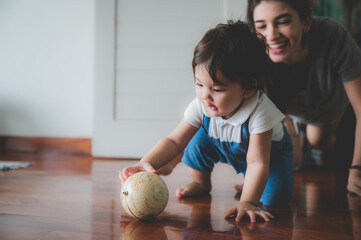 Fototapeta premium Cheerful young mother playing with excited little boy while spending time together and having fun in light room at home