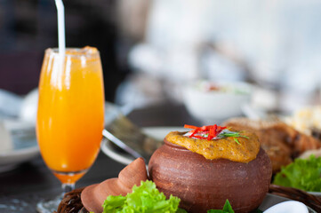 Thai Steamed seafood curry serve in clay pot and fresh orange juice, spicy taste food in Thailand.