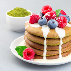Matcha pancakes served with condensed milk, blueberry and raspberry on a white plate, square format
