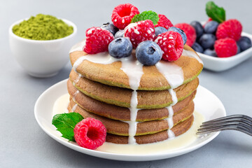 Matcha pancakes served with condensed milk, blueberry and raspberry on white plate, horizontal, closeup