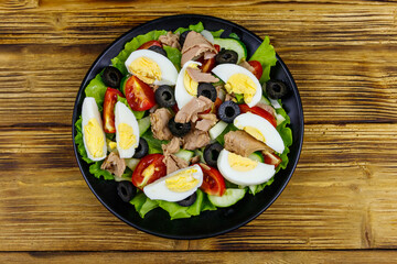 Tasty tuna salad with lettuce, black olives, eggs and fresh vegetables on wooden table. Top view