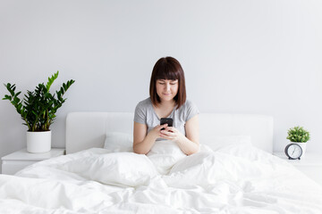 happy woman sitting on bed and using smart phone at home