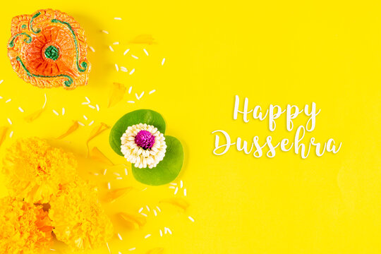 Happy Dussehra festival. Clay diya and flower on yellow paper background with text.