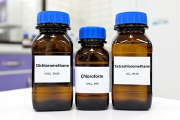 Selective focus of pure dichloromethane, chloroform and tetrachloromethane liquid chemical compound set in dark glass bottles inside a chemistry laboratory with copy space. Set of industrial solvents.