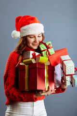 Joyful woman woman holding a lot of boxes with gifts on a gray background.
