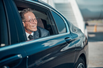 Smiling businessman leaving airport in car with driver