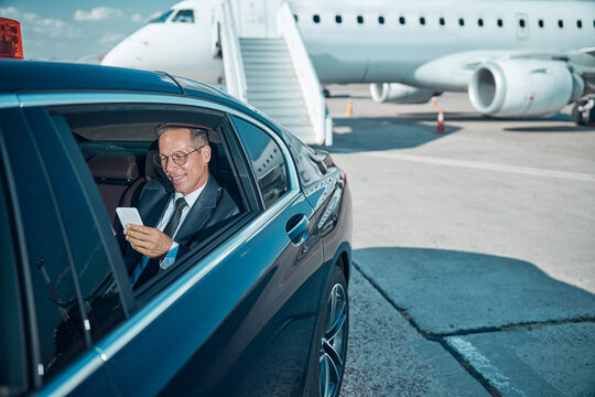 Cheerful businessman with smartphone in car at airport