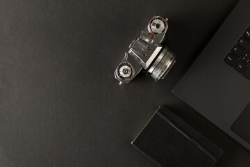 Retro analog SLR camera and notebook next to laptop on black desk in office, digital photography or...