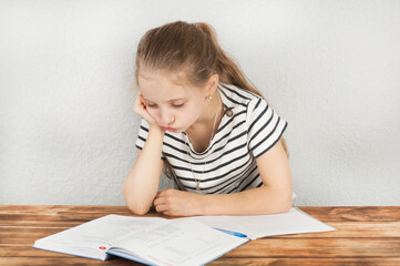 Girl 8 - 10 years old doing homework sitting at a wooden table. Homeschooling